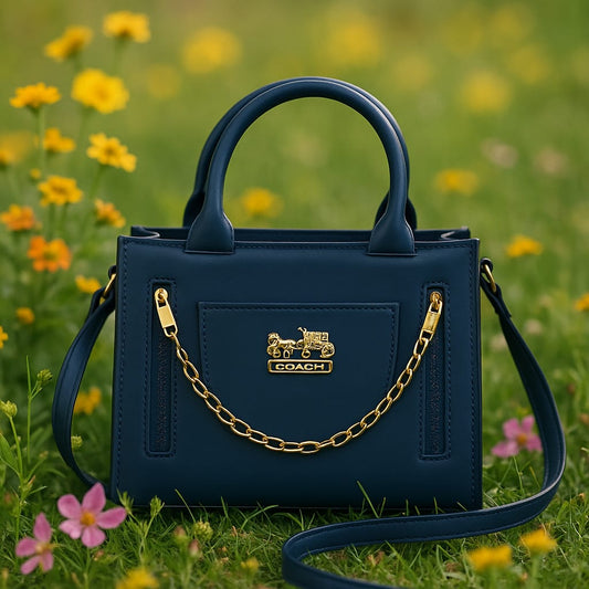 Blue Coach handbag with a gold chain on a grassy background with flowers